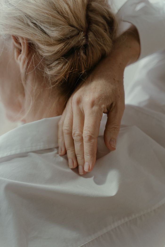 services-02 A peaceful close-up image of a woman touching her neck, wearing a white shirt.